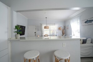 A modern kitchen with a central island, white cabinetry, and two wicker bar stools.