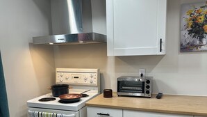 A compact kitchen with white cabinetry, a stainless steel range hood, a built-in oven, a toaster, and a wooden countertop.
