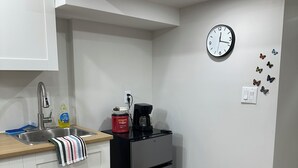 A kitchen with white cabinets, a stainless steel sink, a refrigerator, a clock, and a power outlet.