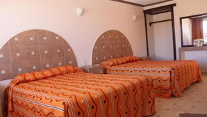 Habitación de hotel con dos camas, cada una con una colcha naranja estampada, un espejo grande y piso de baldosas.