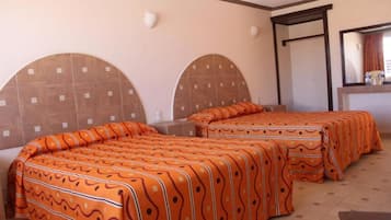 Habitación de hotel con dos camas, cada una con una colcha naranja estampada, un espejo grande y piso de baldosas.