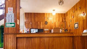 Un mostrador de recepción de madera con un reloj, un cartel de no fumar y una señalización de ruta de evacuación verde.