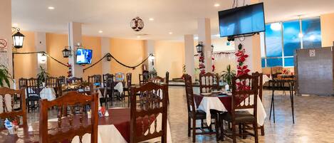 A dining area with multiple tables and chairs, a television mounted on the wall, and decorative lights.