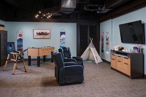 Une pièce équipée d’un baby-foot, de fauteuils inclinables, d’un téléviseur et d’une bibliothèque.