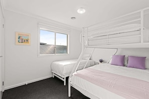 A bedroom with a bunk bed, a single bed, a window with a view, and a small plant on the bedside table. - Scentbark Family Retreat (Surf Coast)