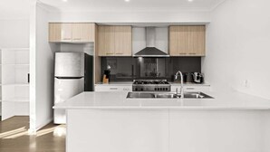A modern kitchen with white cabinetry, a stainless steel sink, and a built-in stove. - Scentbark Family Retreat (Surf Coast)