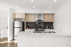A modern kitchen with white cabinetry, a stainless steel sink, and a built-in stove. - Scentbark Family Retreat (Surf Coast)