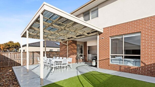 A covered patio with a table and chairs, a brick house, and a lawn. - Scentbark Family Retreat (Surf Coast)