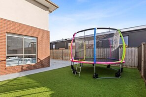 A trampoline in a backyard with a brick house and a wooden fence. - Scentbark Family Retreat (Surf Coast)