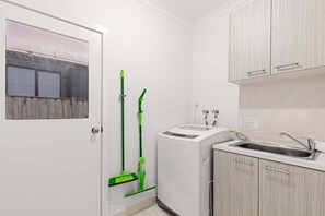 A compact kitchen with a built-in washing machine, a sink, and a door with a window. - Scentbark Family Retreat (Surf Coast)