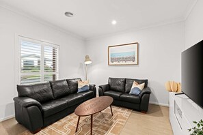 A modern living room with two black leather sofas, a coffee table, a floor lamp, a framed picture on the wall, and a flat-screen TV. - Scentbark Family Retreat (Surf Coast)