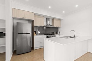 A modern kitchen with white cabinetry, stainless steel appliances, and a central island with a sink. - Scentbark Family Retreat (Surf Coast)