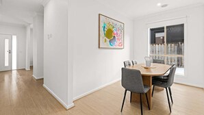 A dining area with a wooden table and chairs, a painting on the wall, and a window with a view. - Scentbark Family Retreat (Surf Coast)