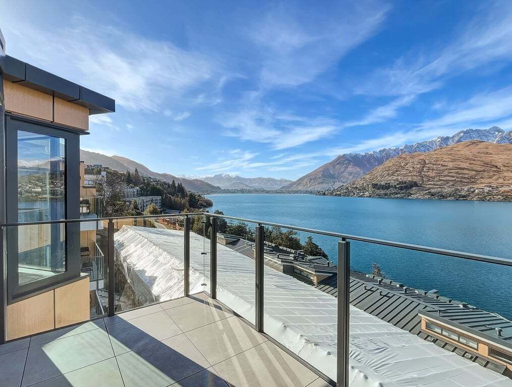 A modern building with a balcony overlooking a lake and mountains.