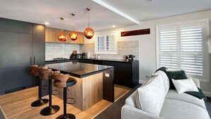 A modern kitchen with a central island, bar stools, pendant lighting, and a view to a living area with a sofa. - Above the Lake | Lakeview Getaway (Queenstown)