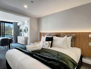 A modern hotel room with a large bed, a wooden headboard, and a view of the mountains through the window. - Above the Lake | Lakeview Getaway (Queenstown)