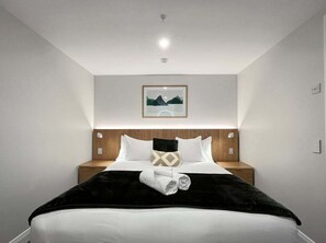 Ein Hotelzimmer mit einem ordentlich bezogenen Bett, einem Kopfteil mit einem Bild und einem Nachttisch mit einer Lampe.