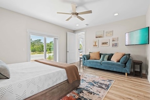 A bedroom with a bed, a blue sofa, a ceiling fan, and a TV mounted on the wall. - Rooftop Retreat w/ Gulf Views + Pool (Inlet Beach)