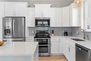 A modern kitchen with white cabinetry, stainless steel appliances, a tiled backsplash, and a wooden floor. - Rooftop Retreat w/ Gulf Views + Pool (Inlet Beach)
