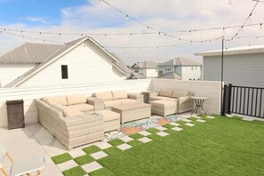 A backyard with a checkered lawn, outdoor furniture, and string lights. - Rooftop Retreat w/ Gulf Views + Pool (Inlet Beach)