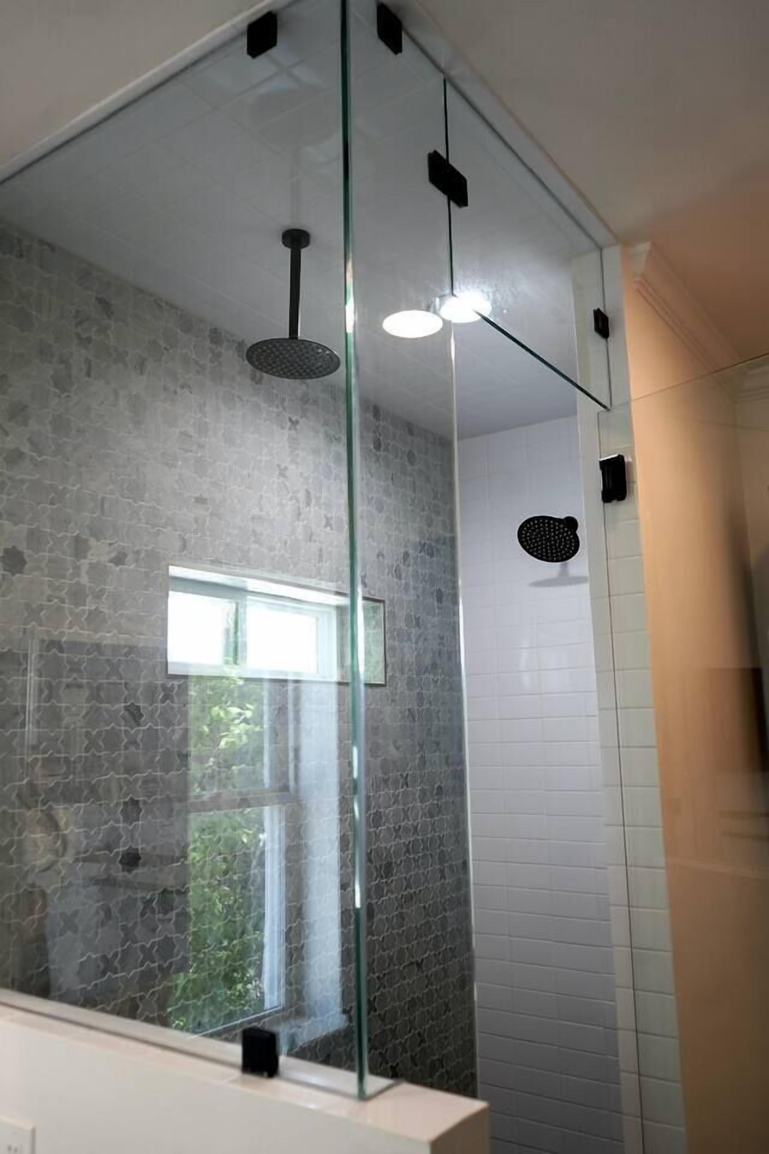 A modern bathroom with a glass shower enclosure, a visible window, and a stone-textured wall.