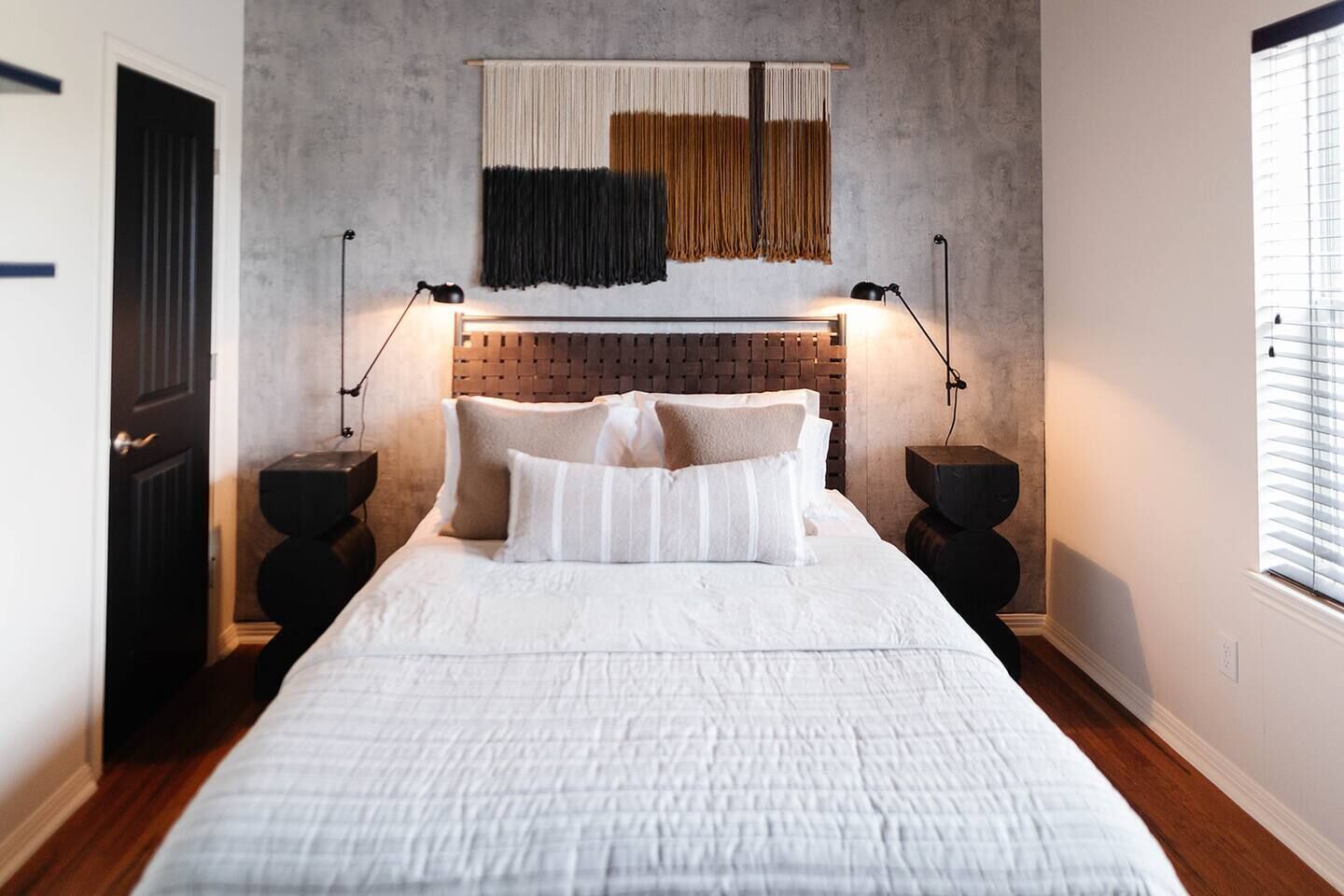 Een slaapkamer met een groot bed, twee nachtkastjes, een hoofdbord met een structuur en een wandtapijt.