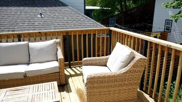 A wooden deck with a wicker sofa and armchair, a small table, and a railing. - Chef's Kitchen · Game Room+Casita · Group Ready! (Austin)