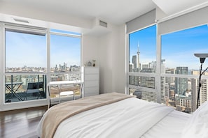 Une chambre moderne dotée d’un grand lit, d’un bureau et d’une chaise, et offrant une vue imprenable sur les toits de la ville grâce à de grandes fenêtres.