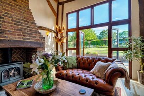 Ein gemütliches Wohnzimmer mit Kamin, Ledersofa und großen Fenstern mit Blick auf einen Garten.