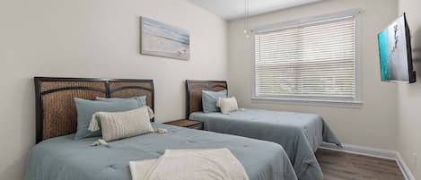 Un dormitorio con dos camas, un ventilador de techo, una ventana con persianas y un cuadro en la pared.