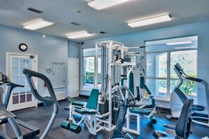 A gym with various exercise equipment, large windows, and a clock on the wall. - The Cayman House: Steps from Beach | Pool & Clubhouse Amenities (Destin)