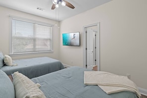 A bedroom with two beds, a ceiling fan, a television, and a door. - The Cayman House: Steps from Beach | Pool & Clubhouse Amenities (Destin)