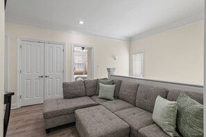 A living room with a sectional sofa, a door, a ceiling fan, and a window. - The Cayman House: Steps from Beach | Pool & Clubhouse Amenities (Destin)