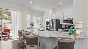 A modern kitchen with a marble island, stainless steel appliances, and a seating area with bar stools. - The Cayman House: Steps from Beach | Pool & Clubhouse Amenities (Destin)