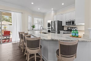 A modern kitchen with a marble island, stainless steel appliances, and a seating area with bar stools. - The Cayman House: Steps from Beach | Pool & Clubhouse Amenities (Destin)