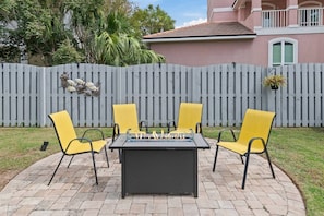 A patio with a fire pit table and four yellow chairs. - The Cayman House: Steps from Beach | Pool & Clubhouse Amenities (Destin)