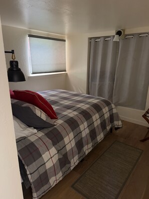 Ein Schlafzimmer mit einem Bett, einem Fenster mit Jalousien, einer Lampe und einem Vorhang.
