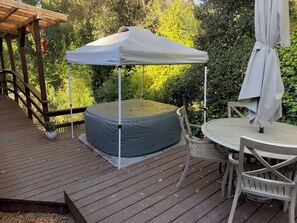 Eine Holzterrasse mit rundem Tisch und Stühlen, einem überdachten Sitzbereich und einer Pergola.