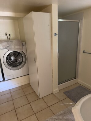Ein Waschbereich mit Waschmaschine, hohem Schrank und Duschkabine.