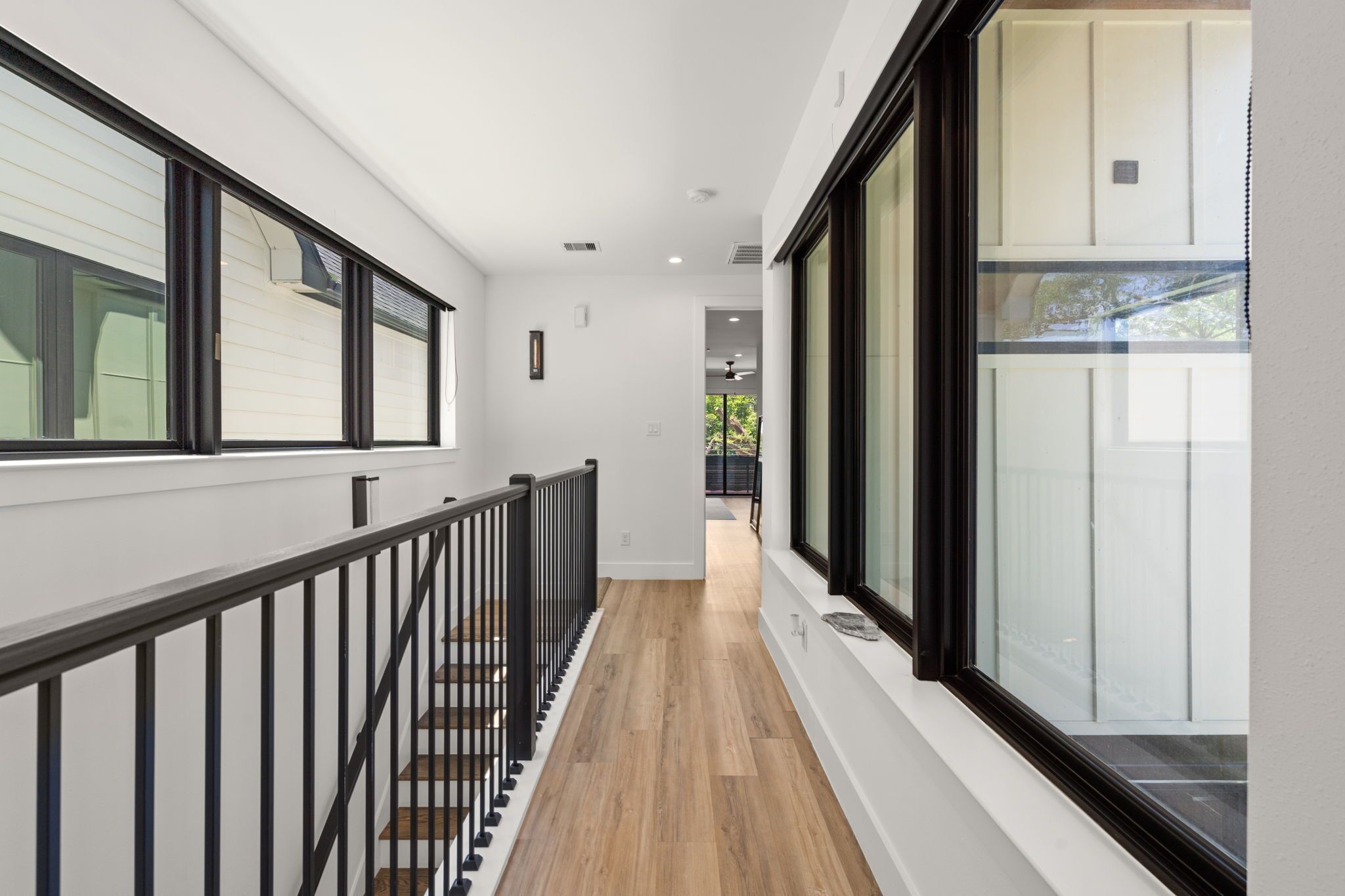 A corridor with a wooden floor, black railing, and large windows on both sides.