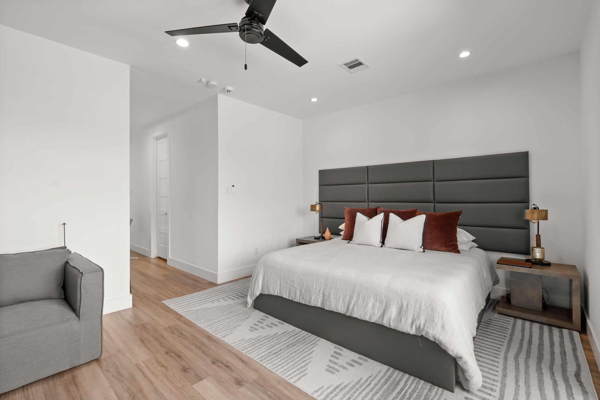 Een moderne slaapkamer met een bed, nachtkastjes, een plafondventilator en een grijze bank.