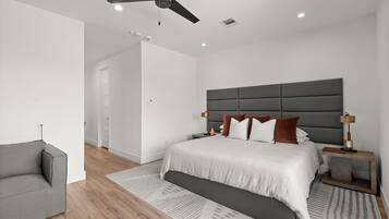 Een moderne slaapkamer met een bed, nachtkastjes, een plafondventilator en een grijze bank.