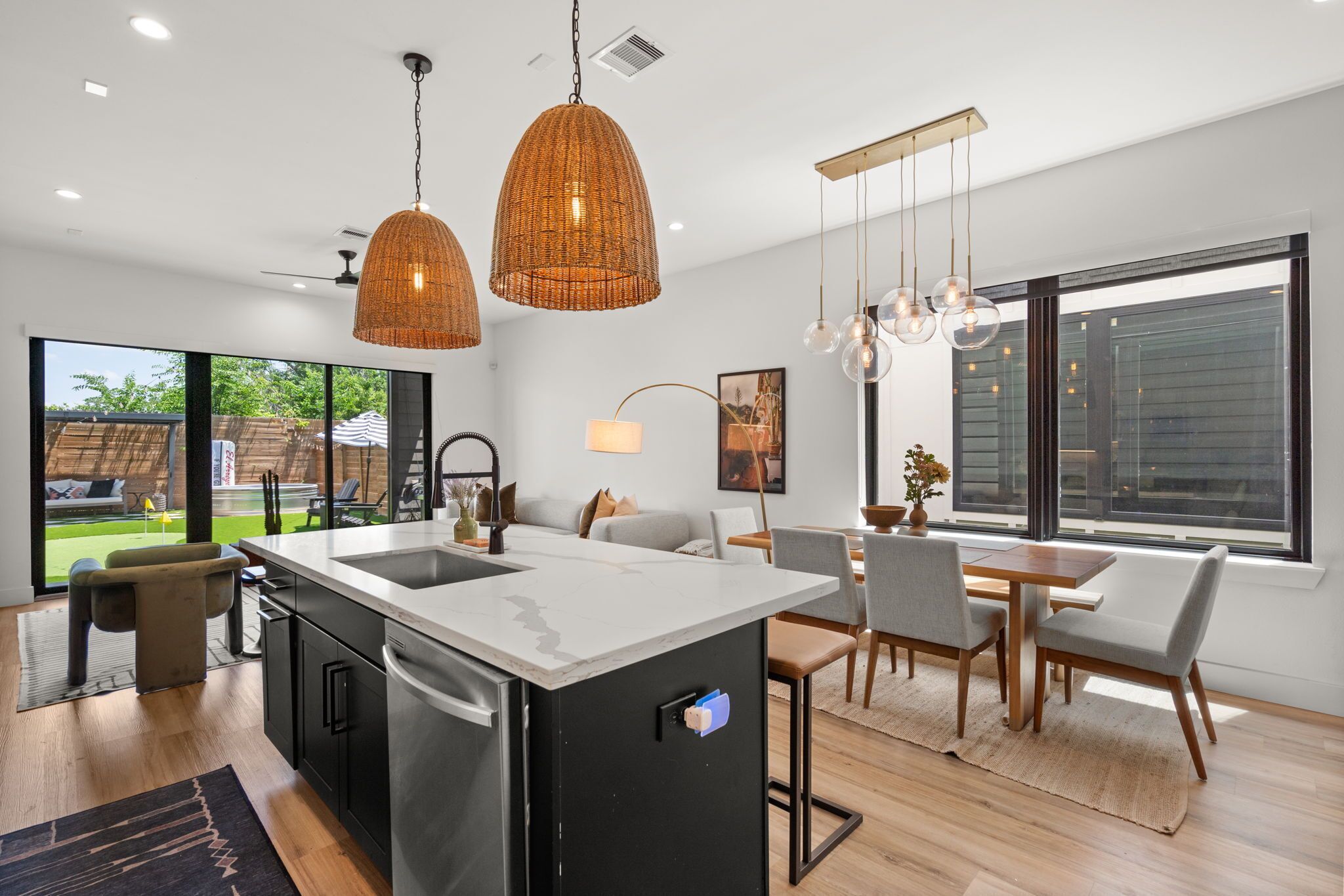 Una cocina moderna con una isla central, un comedor con mesa y sillas, y ventanas amplias que dejan entrar luz natural.