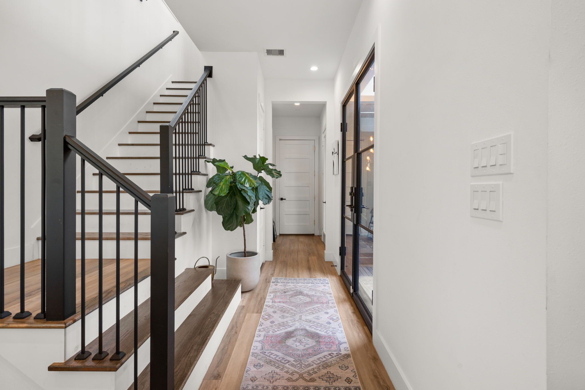 Un intérieur moderne avec un escalier, une plante en pot et un tapis à motifs.