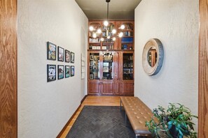 A hallway with a wooden bench, a herringbone-patterned rug, a wooden bookshelf, and framed pictures on the wall. - Nomad Lodge - 5 Bedroom Nature & Travel Inspired Home, Centrally Located (Wasilla)
