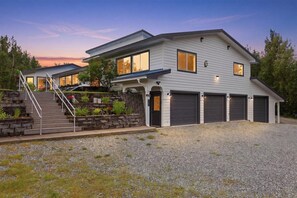 A two-story house with a garage, a staircase, and a landscaped front yard. - Nomad Lodge - 5 Bedroom Nature & Travel Inspired Home, Centrally Located (Wasilla)
