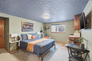 A bedroom with a bed, bedside tables, a desk, a chair, a television, and a window. - Nomad Lodge - 5 Bedroom Nature & Travel Inspired Home, Centrally Located (Wasilla)