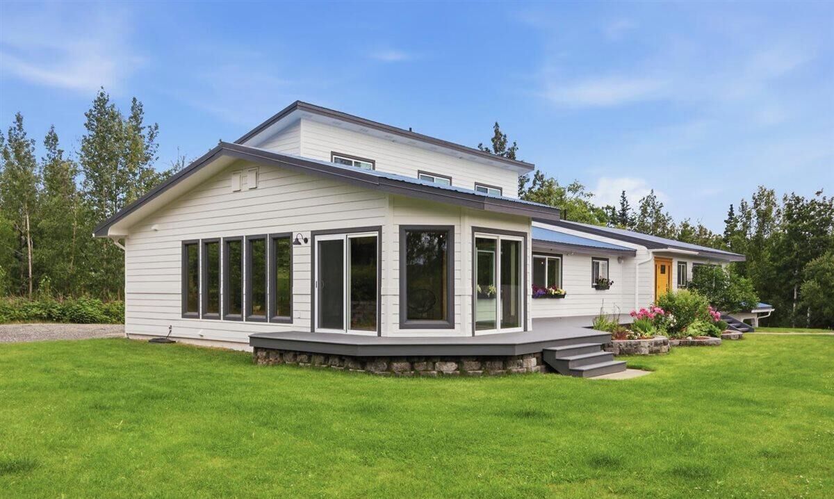 Ein zweistöckiges Haus mit überdachter Veranda, großen Fenstern und einem gepflegten Rasen.