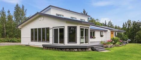 Ein zweistöckiges Haus mit überdachter Veranda, großen Fenstern und einem gepflegten Rasen.