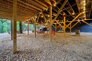 An open-air pavilion with wooden beams and string lights, gravel flooring, picnic tables, and a sign indicating a nature reserve. - Peaceful Easy Feeling · Woodland Retreat: Hot Tub, Swing Chairs, Fire Pit (Broken Bow)